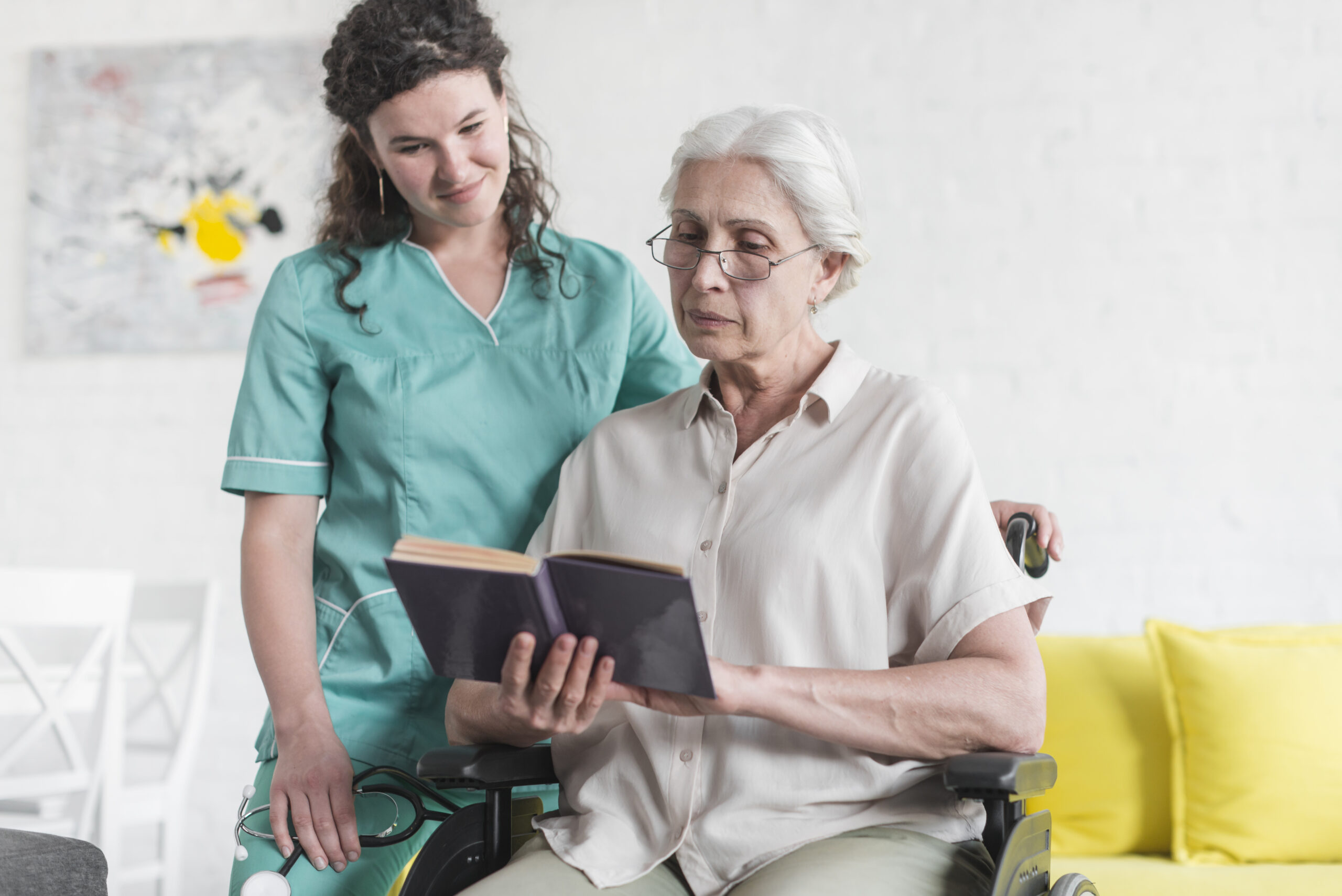 senior woman sitting wheelchair reading book with nurse standing